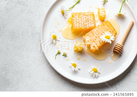 Golden honeycomb on white plate with chamomile flowers, fresh honey 141563895