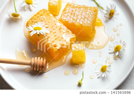 Golden honeycomb on white plate with chamomile flowers, fresh honey Golden honeycomb on white plate with chamomile flowers, fresh honey 141563896