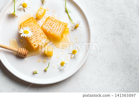 Golden honeycomb on white plate with chamomile flowers, fresh honey Golden honeycomb on white plate with chamomile flowers, fresh honey 141563897
