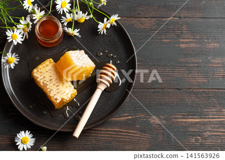 Golden honeycomb on white plate with chamomile flowers, fresh honey Golden honeycomb on white plate with chamomile flowers, fresh honey 141563926