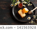 Golden honeycomb on black plate with chamomile flowers, fresh honey 141563928
