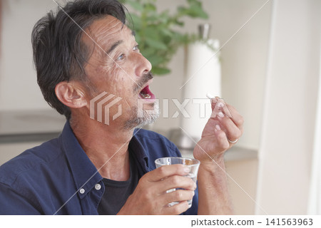 A senior man attempting to take oral medication. A senior man attempting to take oral medication. 141563963