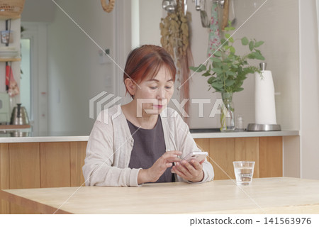 一位老年婦女在燈光明亮的房間裡使用智慧型手機。 141563976