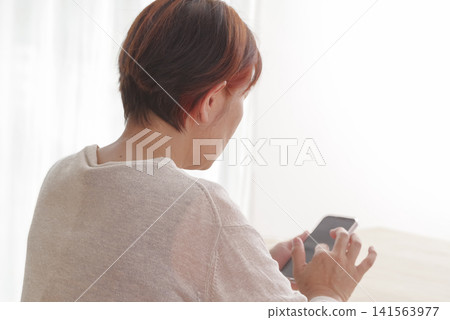 A senior woman operating her smartphone in a brightly lit room. A senior woman operating her smartphone in a brightly lit room. 141563977
