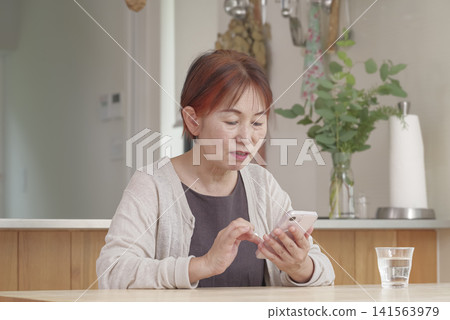 A senior woman operating her smartphone in a brightly lit room. A senior woman operating her smartphone in a brightly lit room. 141563979