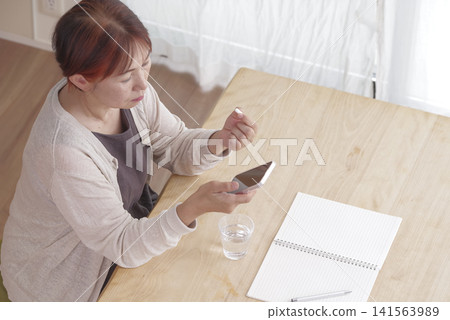A woman manages her health using her smartphone and pills. 141563989
