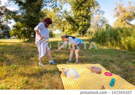Young Caucasian girl and her mother using anti-mosquito spray in a sunny park enjoying nature while preventing insect bites during tick season. Wide shot Young Caucasian girl and her mother using anti-mosquito spray in a sunny park enjoying nature while preventing insect bites during tick season. Wide shot 141564107