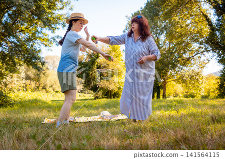 Caucasian mother and daughter applying mosquito repellent together in a summer park staying safe from ticks and insects while enjoying family time outdoors. Mid shot 141564115