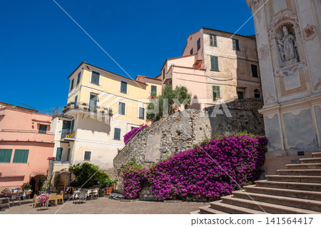 Cervo, liguria, italy. June 22, 2025. Charming cervo village public square with traditional ligurian architecture, bougainvillea flowers, and church details under a clear blue sky Cervo, liguria, italy. June 22, 2025. Charming cervo village public square with traditional ligurian architecture, bougainvillea flowers, and church details under a clear blue sky 141564417
