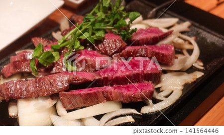 close up of Sizzling rare steak slices served on a hot iron plate with caramelized onions and fresh green garnish with copy space close up of Sizzling rare steak slices served on a hot iron plate with caramelized onions and fresh green garnish with copy space 141564446