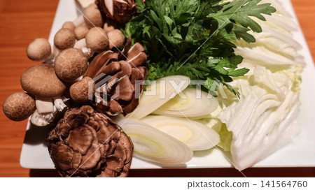 close up of fresh Japanese hot pot shabushabu ingredients beautifully arranged on a white plate, including Shiitake, shimeji mushrooms, crisp chrysanthemum greens, sliced leeks, napa cabbage and tofu. close up of fresh Japanese hot pot shabushabu ingredients beautifully arranged on a white plate, including Shiitake, shimeji mushrooms, crisp chrysanthemum greens, sliced leeks, napa cabbage and tofu. 141564760