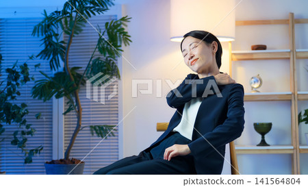 A female business person relaxing in a darkened room. Stress, fatigue, stiff shoulders, break, overtime, going home, night, unwinding. A female business person relaxing in a darkened room. Stress, fatigue, stiff shoulders, break, overtime, going home, night, unwinding. 141564804