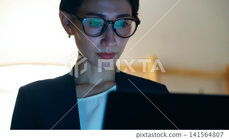 A middle-aged woman looking at a computer screen in a darkened room. Overtime, night, office, work, tasks, SE, engineer, screen, development. A middle-aged woman looking at a computer screen in a darkened room. Overtime, night, office, work, tasks, SE, engineer, screen, development. 141564807