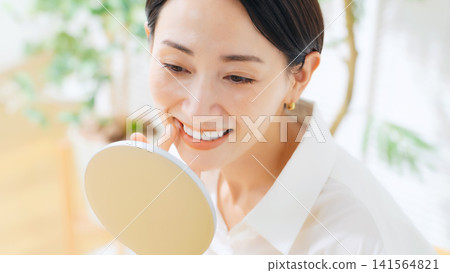A middle-aged woman checks her teeth in the mirror. Whitening, implants, cavity treatment, dentistry, dental care, white teeth. A middle-aged woman checks her teeth in the mirror. Whitening, implants, cavity treatment, dentistry, dental care, white teeth. 141564821