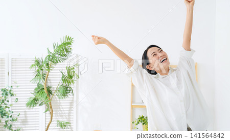 一位中年婦女在房間裡歡呼雀躍。她快樂、喜悅、開心、精力充沛、積極向上、放鬆自在、微笑、心滿意足。 一位中年婦女在房間裡歡呼雀躍。她快樂、喜悅、開心、精力充沛、積極向上、放鬆自在、微笑、心滿意足。 141564842