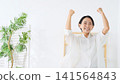 A middle-aged woman makes a triumphant gesture in her room. Happy, delighted, having fun, energetic, positive, relaxed, smiling, satisfied. 141564843