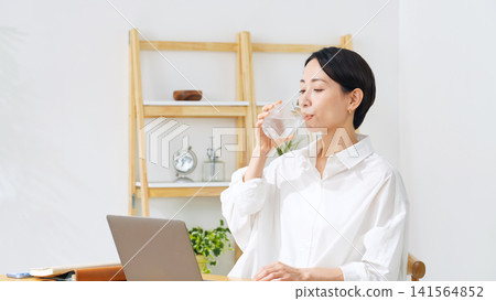 一位中年婦女正在喝水。放鬆、補水、舒緩身心、辦公室、服藥、藥品、健康、醫療保健、醫療。 一位中年婦女正在喝水。放鬆、補水、舒緩身心、辦公室、服藥、藥品、健康、醫療保健、醫療。 141564852