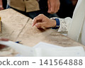 A close-up capture of a traditional wedding ceremony moment, highlighting the groom seated beside the officiant  141564888