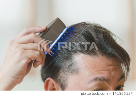 Close-up of a man's head as he applies a blue LED brush to his forehead. 141565134