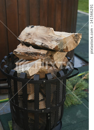 Firewood stacked high in metal basket on outdoor patio surface. Natural wood logs for heating, organized storage, backyard environment, home energy supply, rustic lifestyle concept. vertical Firewood stacked high in metal basket on outdoor patio surface. Natural wood logs for heating, organized storage, backyard environment, home energy supply, rustic lifestyle concept. vertical 141566291