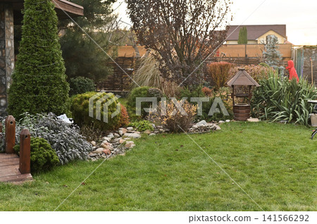 Garden with decorative stones and trimmed trees, organized environment. green grass enhances beauty of well-arranged landscaping. scenic garden with decorative trees and flowers along stone path. Garden with decorative stones and trimmed trees, organized environment. green grass enhances beauty of well-arranged landscaping. scenic garden with decorative trees and flowers along stone path. 141566292