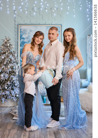 a family in elegant light-blue and white attire opening a gift in a magical winter wonderland a family in elegant light-blue and white attire opening a gift in a magical winter wonderland 141566638