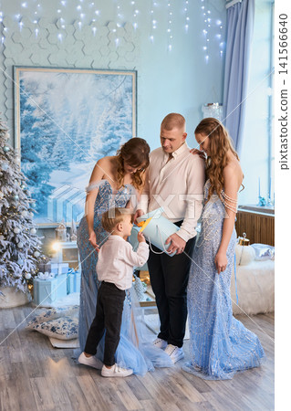 a family in elegant light-blue and white attire opening a gift in a magical winter wonderland a family in elegant light-blue and white attire opening a gift in a magical winter wonderland 141566640
