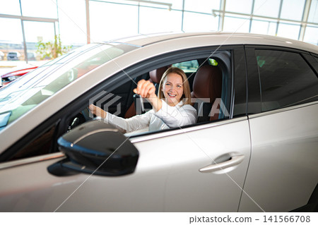 Happy woman holding car key in new vehicle showroom Happy woman holding car key in new vehicle showroom 141566708