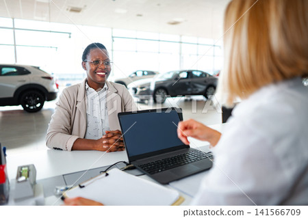 Female customer discussing car purchase with saleswoman at dealership Female customer discussing car purchase with saleswoman at dealership 141566709