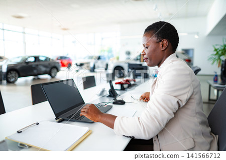 Black businesswoman working on laptop in car dealership Black businesswoman working on laptop in car dealership 141566712