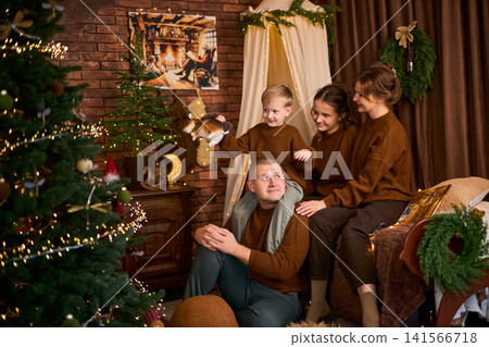 family in matching brown sweaters enjoying a magical moment by the Christmas tree, with a soft-focus family in matching brown sweaters enjoying a magical moment by the Christmas tree, with a soft-focus 141566718