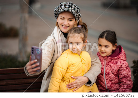 Mother and daughters taking selfie together on park bench Mother and daughters taking selfie together on park bench 141566752