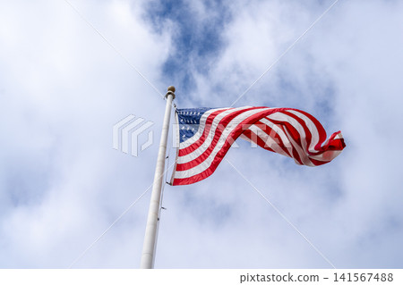 American flag waving on a tall pole against a cloudy sky American flag waving on a tall pole against a cloudy sky 141567488