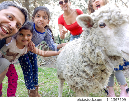 Large family posing for selfie with pet sheep outdoors 141567509