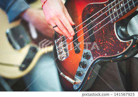 Close-up of Hand Playing Electric Bass Guitar Strings 141567925