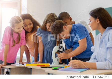 Curious schoolboy looking through microscope while classmates observe during science lesson Curious schoolboy looking through microscope while classmates observe during science lesson 141567968