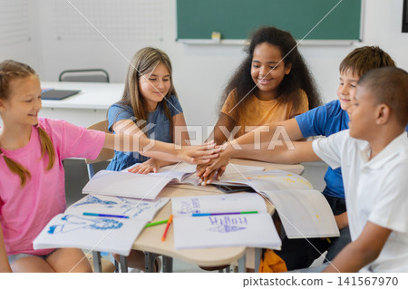 Five diverse schoolchildren stack their hands together over notebooks after group work Five diverse schoolchildren stack their hands together over notebooks after group work 141567970