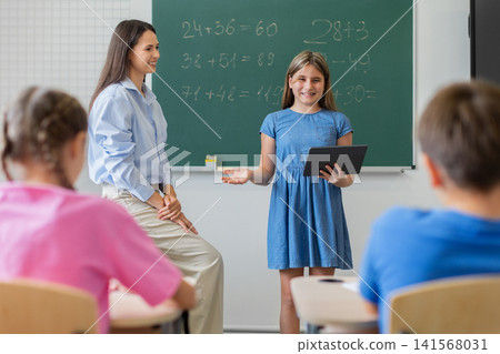 Confident schoolgirl using tablet to present mathematics work to classmates Confident schoolgirl using tablet to present mathematics work to classmates 141568031