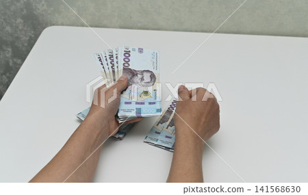 Young woman counts cash money over white desk surface. Young woman counts cash money over white desk surface. 141568630