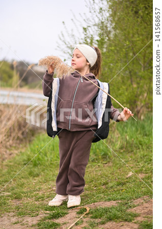 Little girl exploring lakeside nature holding dry reed near calm water. Little girl exploring lakeside nature holding dry reed near calm water. 141568657