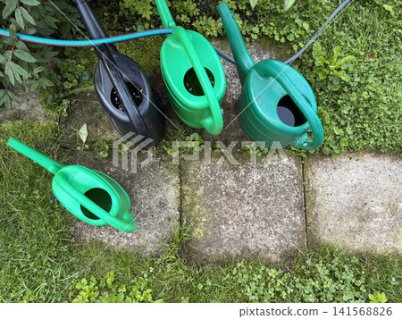 Top View Of Watering Cans And Hose In Home Garden - illustrating gardening, watering plants, home garden maintenance, and outdoor tools. 141568826