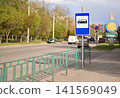 Bus stop sign near urban road with sidewalk barrier and traffic. 141569049