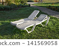Park seating area with sun loungers on green lawn. 141569058