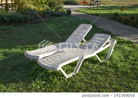Park seating area with sun loungers on green lawn. 141569058
