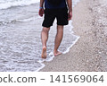 Barefoot person walking along shoreline with waves touching feet, 141569064