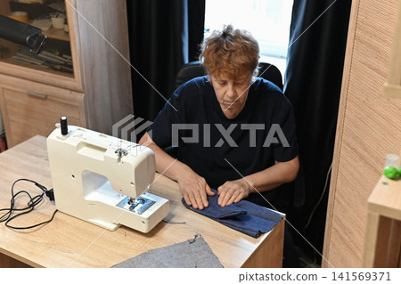 Senior woman sewing at home. Startup small business designer, service. Senior woman sewing at home. Startup small business designer, service. 141569371