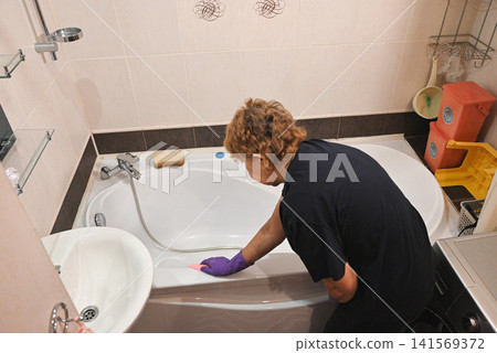 Woman cleaning bathtub in bathroom during afternoon 141569372