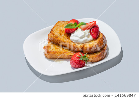 Brioche toasts with strawberries and whipped cream, drizzled with honey on a plate Brioche toasts with strawberries and whipped cream, drizzled with honey on a plate 141569847