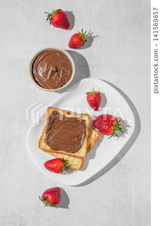 Toasted bread with chocolate cream and strawberry on a plate on a concrete background Toasted bread with chocolate cream and strawberry on a plate on a concrete background 141569857