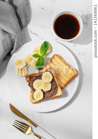Toasted bread with chocolate cream and banana on a plate on a marble background Toasted bread with chocolate cream and banana on a plate on a marble background 141569861